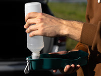 Person using a portable pet water bottle, ideal for travel. Available on all-in-1store.com for easy hydration on the go.